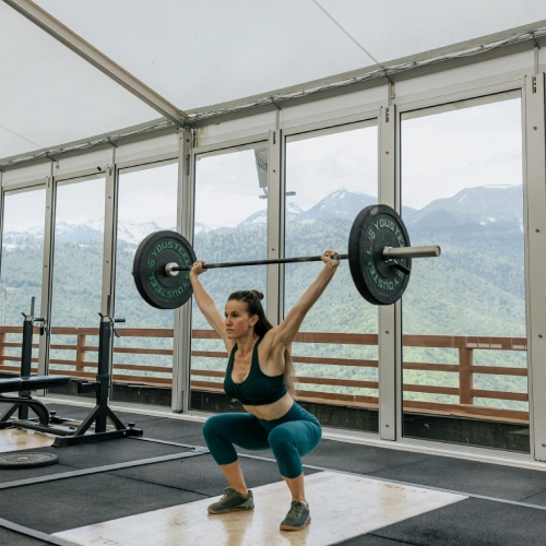 A woman squats with a barbell in a gym at The CompoundCT, Inc. in Stamford, CT, demonstrating strength training.