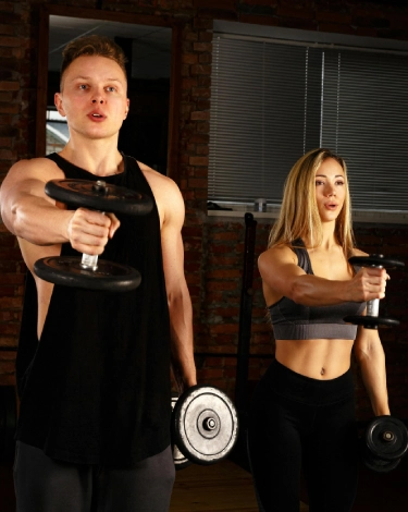 A man and woman lifting dumbbells together in a semi-private gym setting in Stamford, CT.