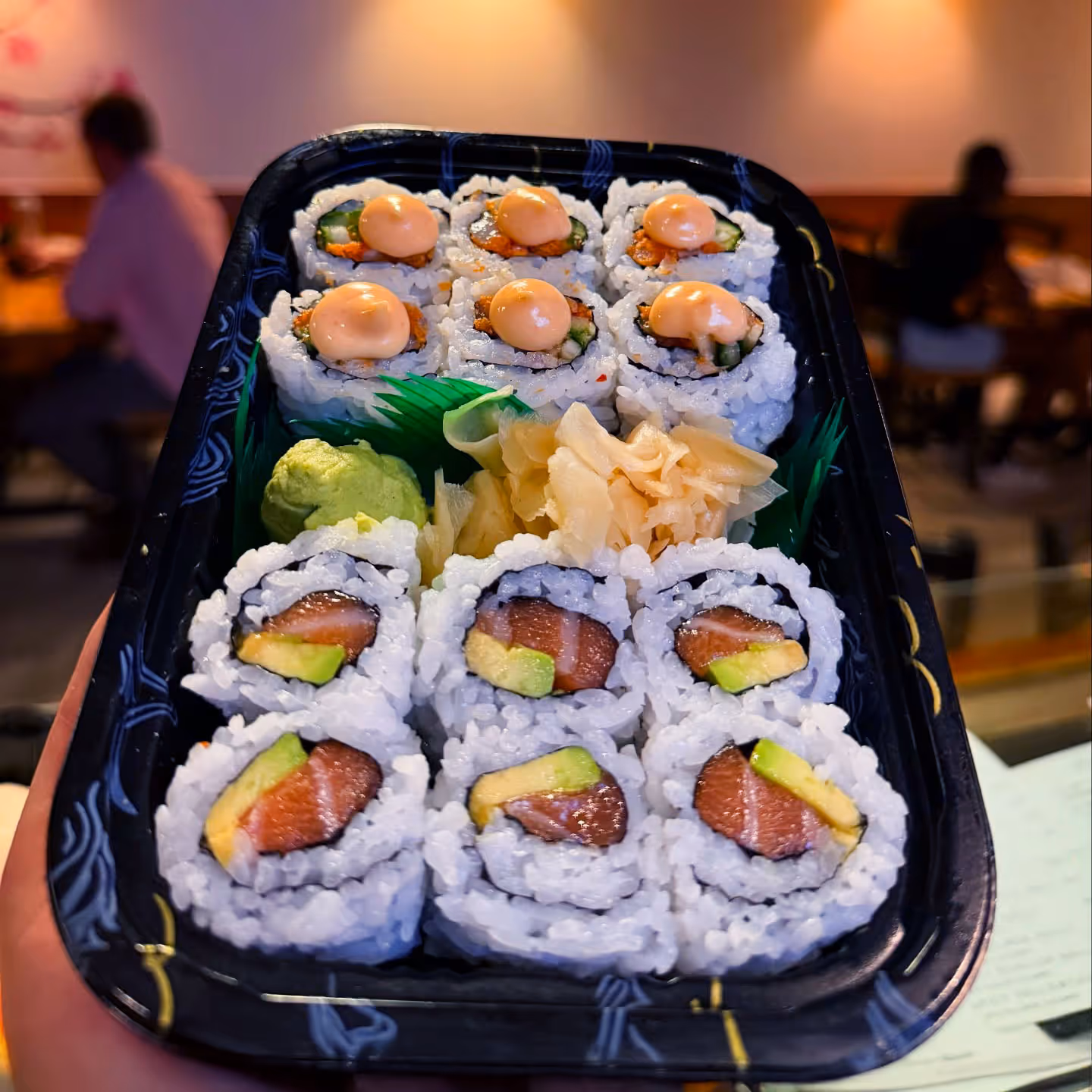 A person holding a tray of assorted sushi.