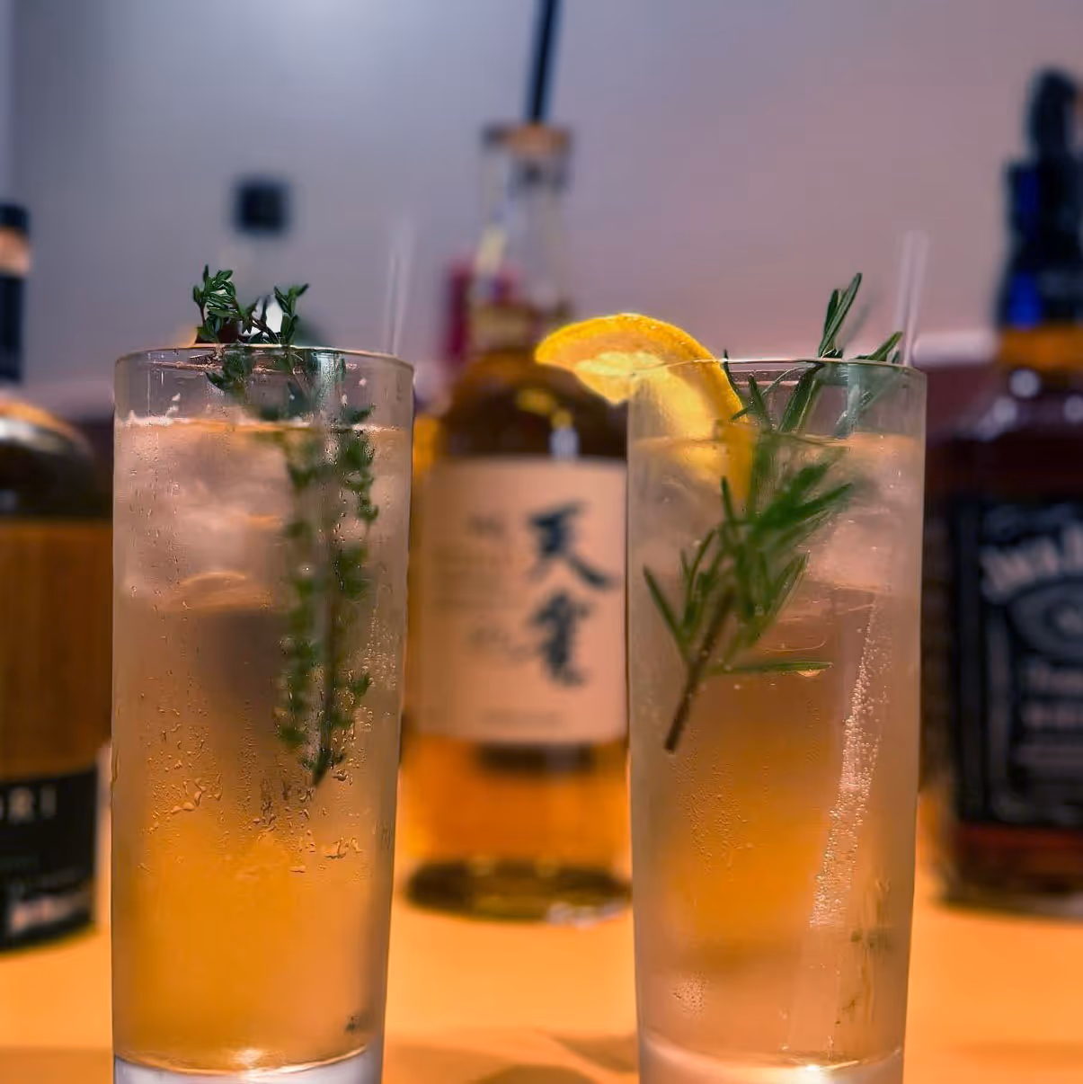 Two drinks with garnishes sit on a table.