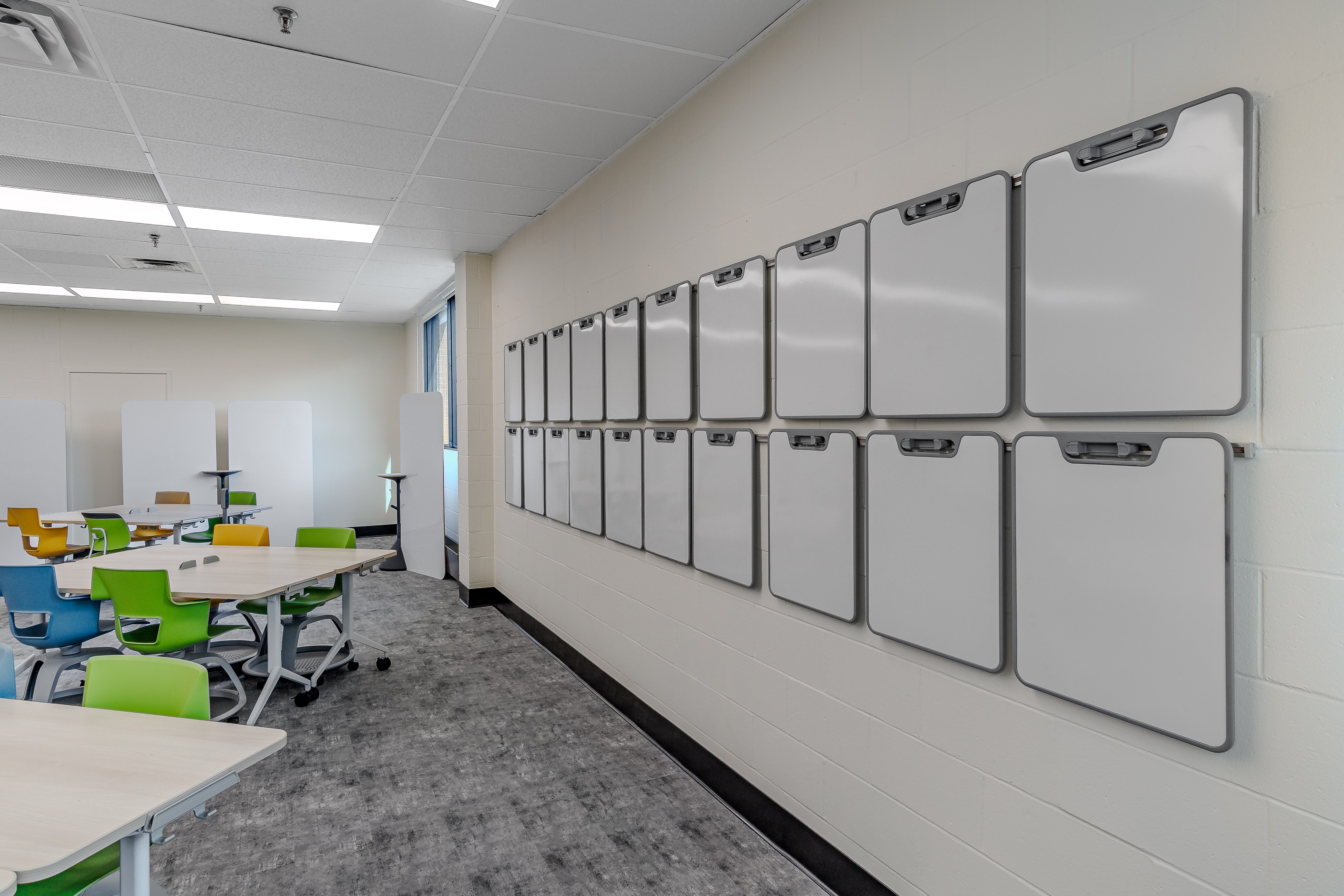 Modern classroom with empty colorful chairs, tables on wheels, and two rows of blank whiteboards mounted on the wall.