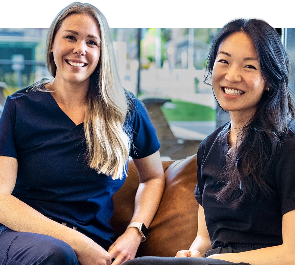 Two SMiiL Heights dental hygienists sitting on cozy clinic couch smiling and chatting