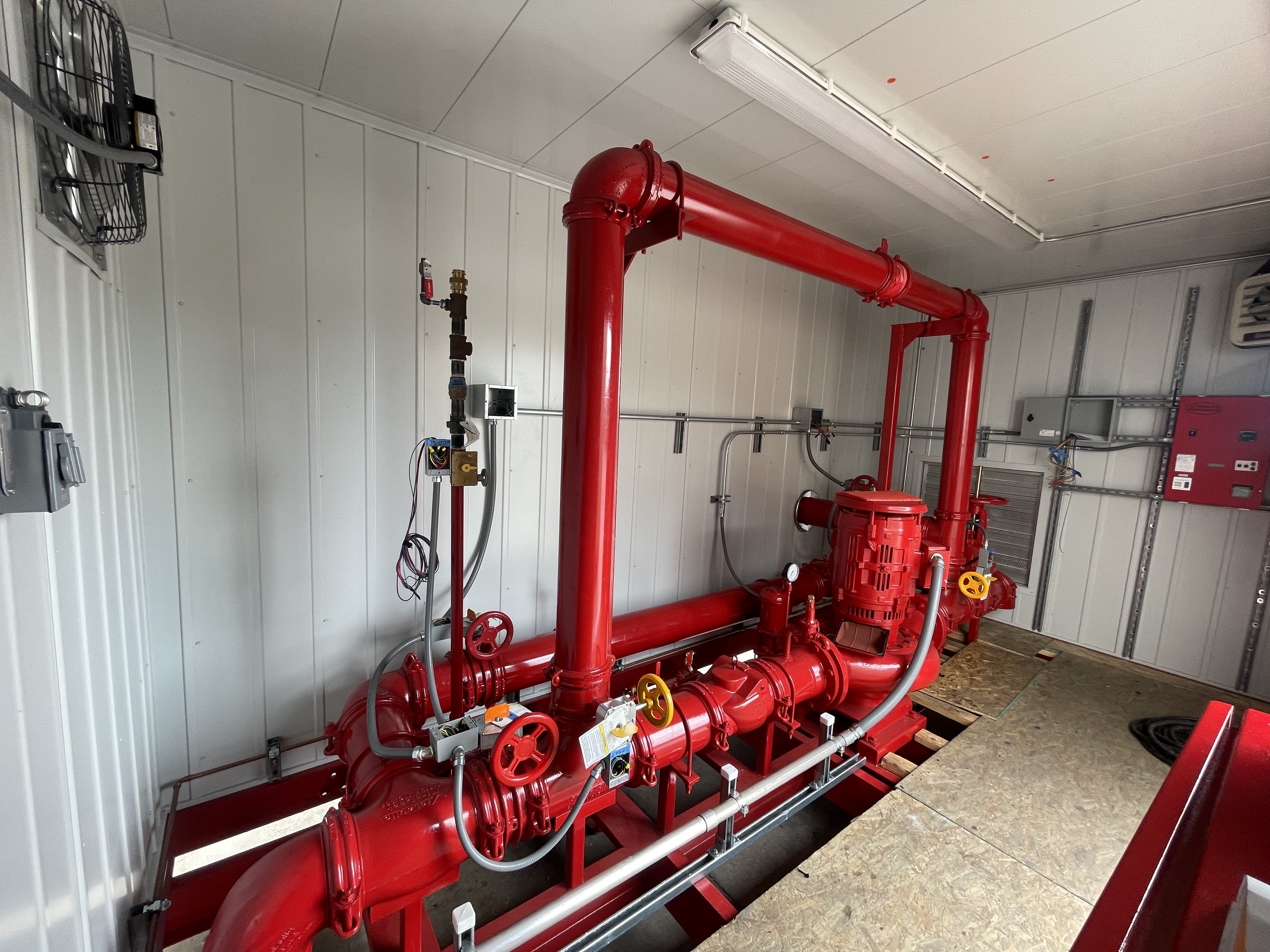 Red industrial piping and pumps system installed inside a white-paneled utility room.