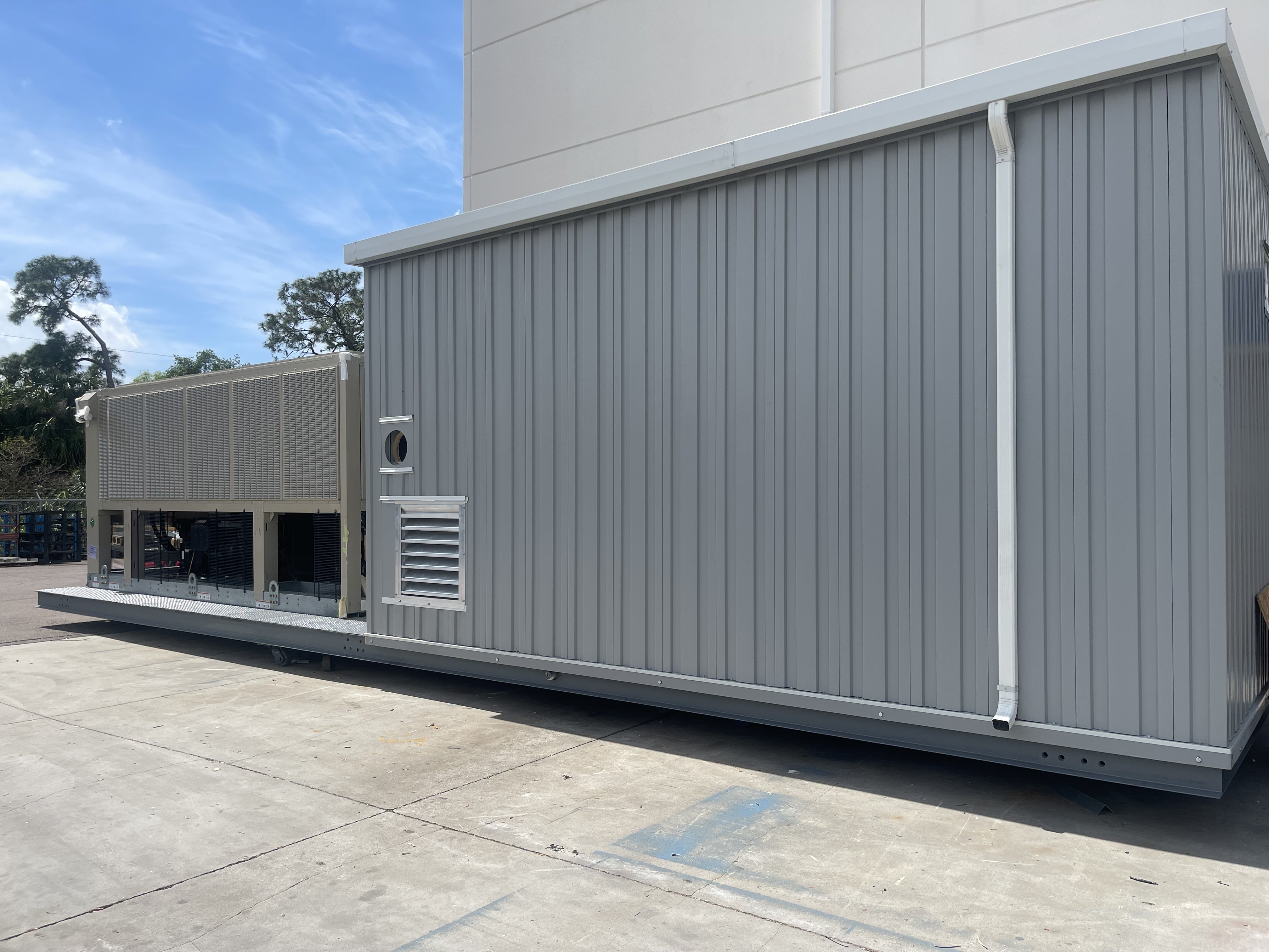 Large grey metal industrial container or equipment unit on concrete surface outside under blue sky.