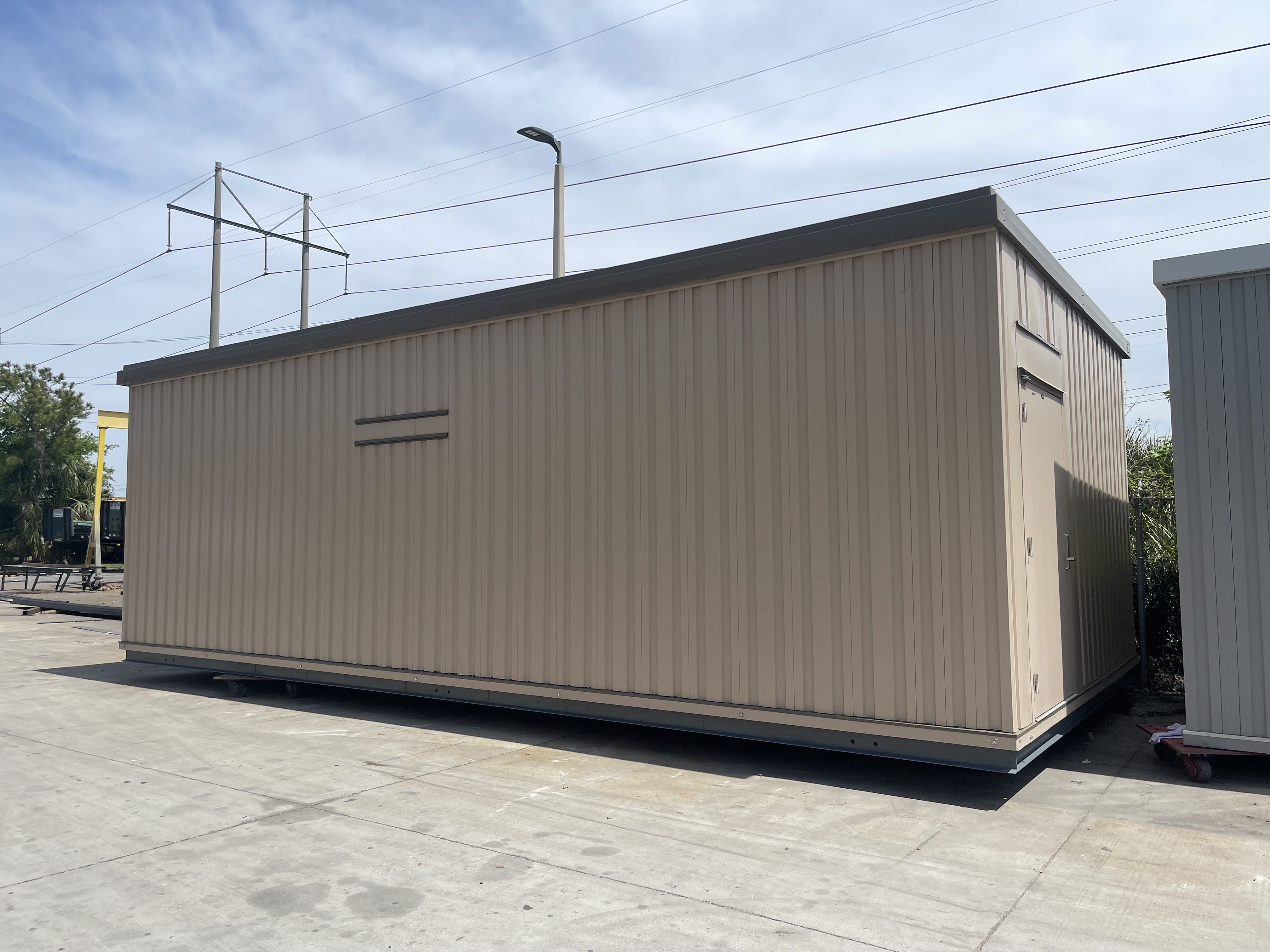 Large beige metal storage container with a door on a concrete surface outdoors.