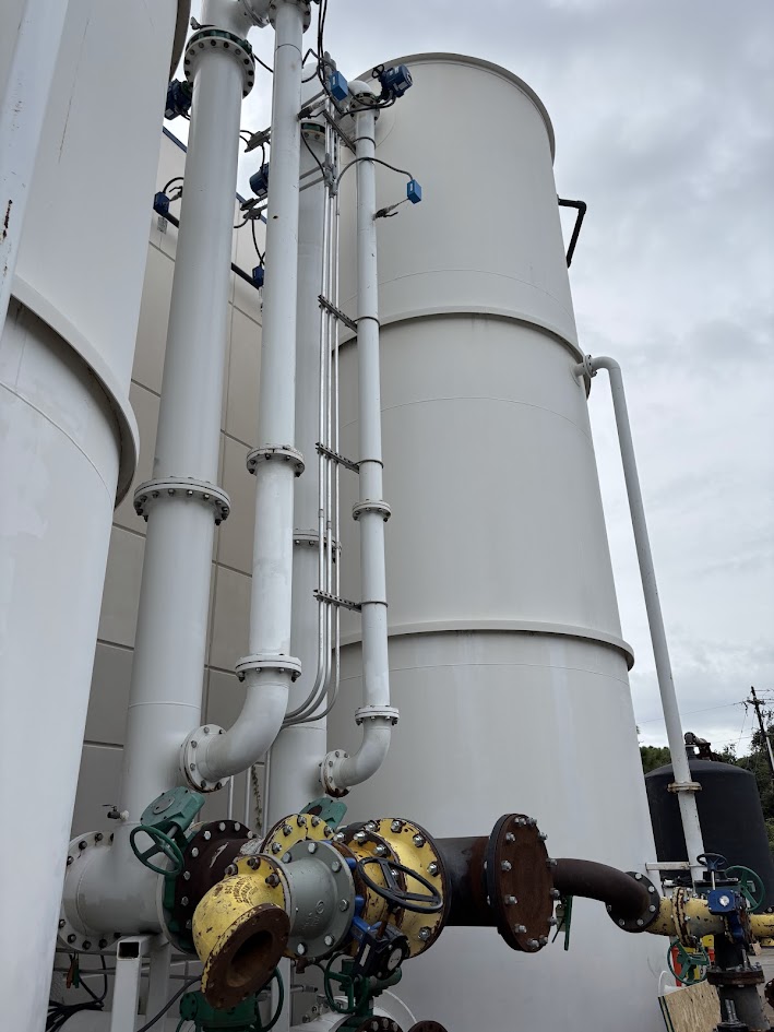 Industrial white storage tanks with attached large white pipes and yellow valve fixtures outdoors.