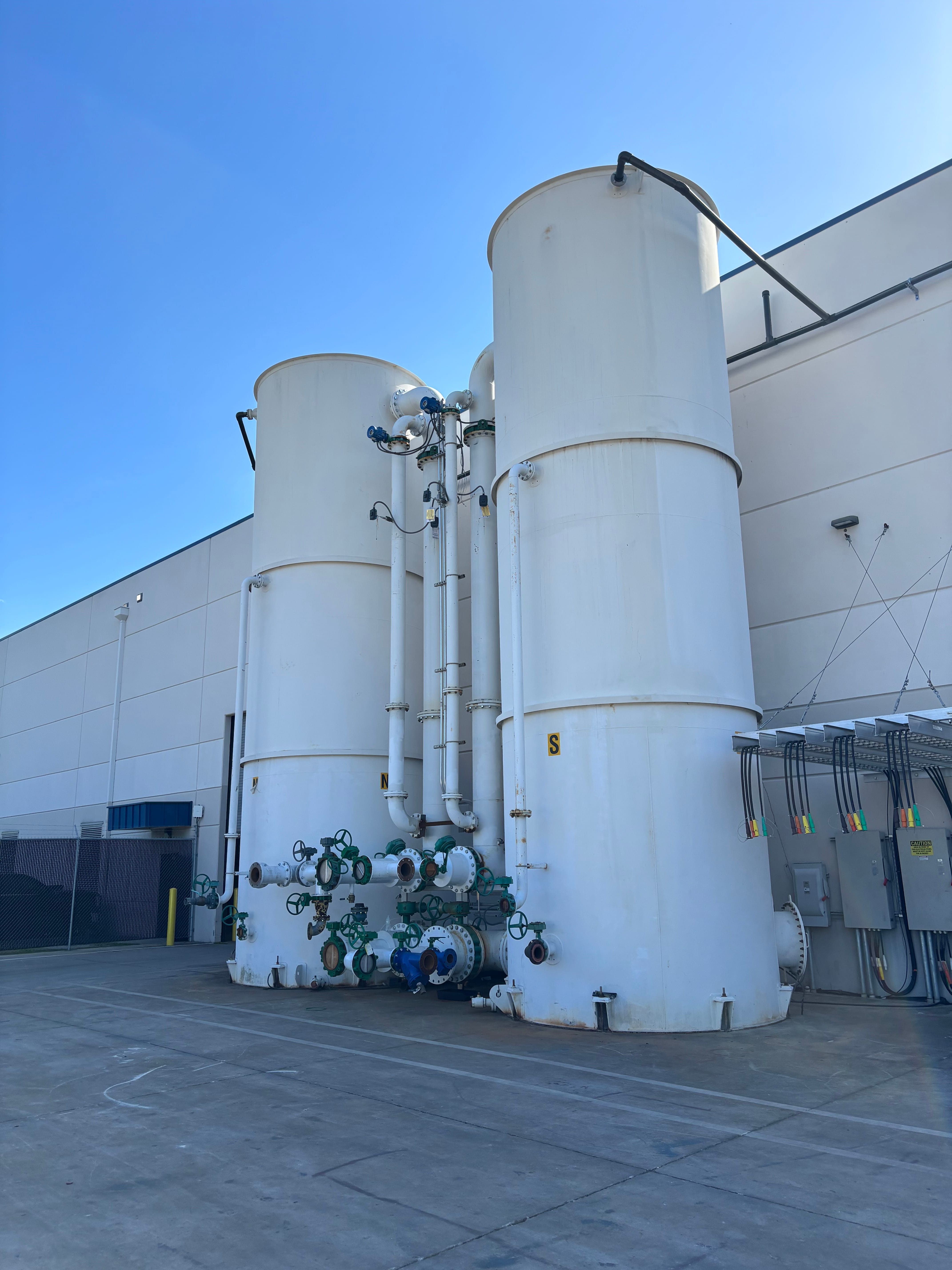Two large white industrial water tanks with valves and pipes outside a building under clear blue sky.