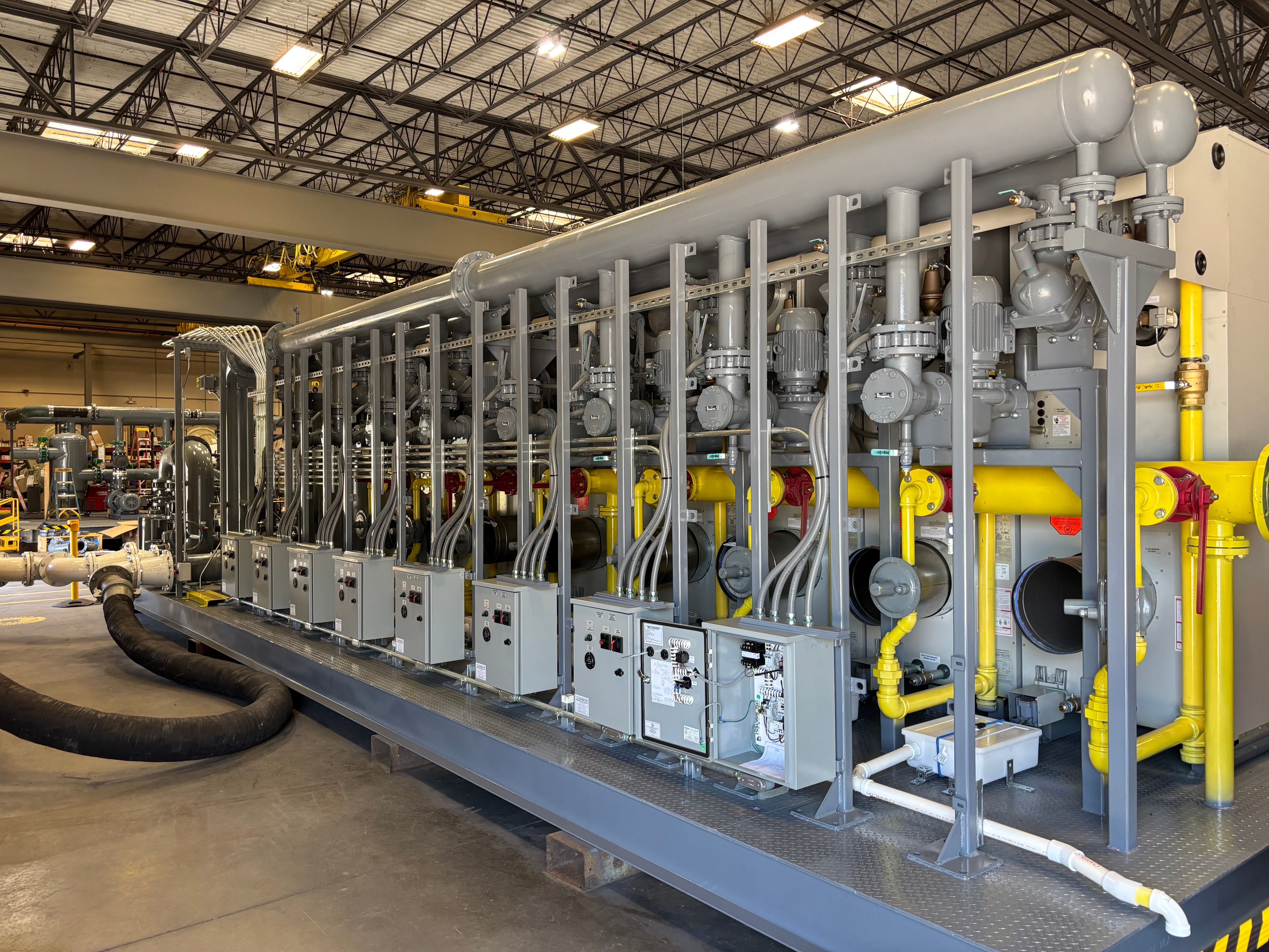 Large industrial machine with gray and yellow pipes, control boxes, and hoses inside a warehouse.