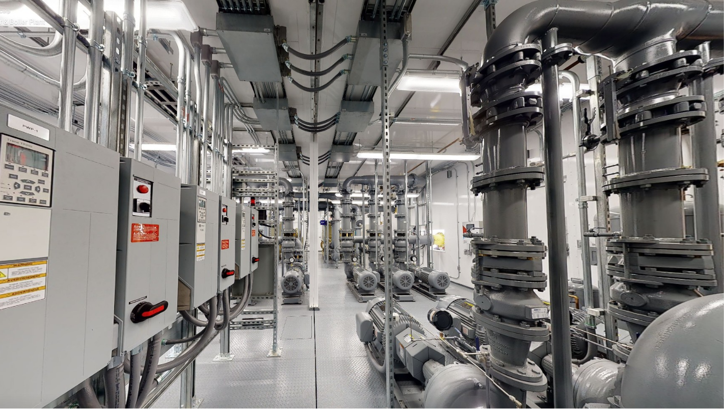 Industrial room with large pipes, control panels, and mechanical equipment for heating or ventilation.