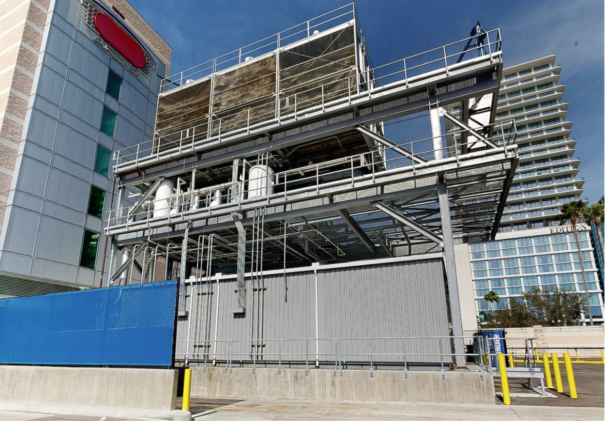 Industrial cooling tower structure with pipes and metal framework outside a building under blue sky.