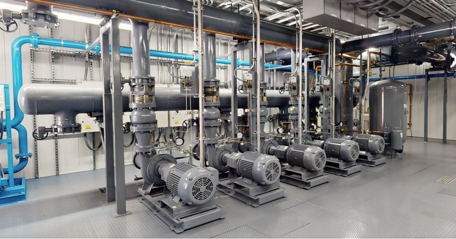 Row of large industrial pumps with connected pipes inside a clean mechanical room.
