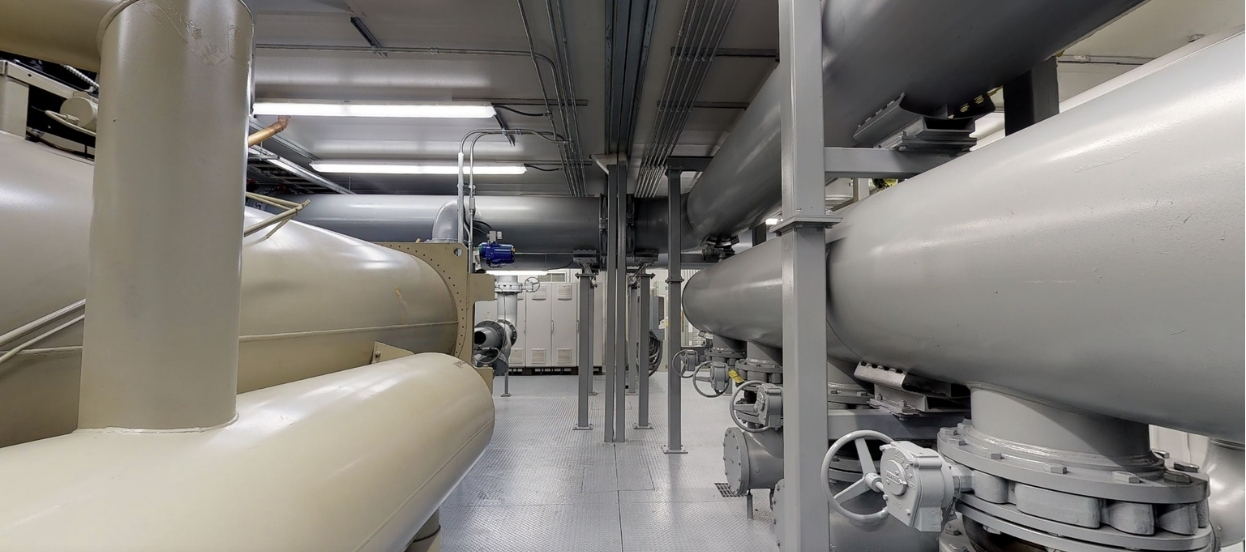 Industrial room with large gray and beige pipes and metal valves lining both sides of the walkway.