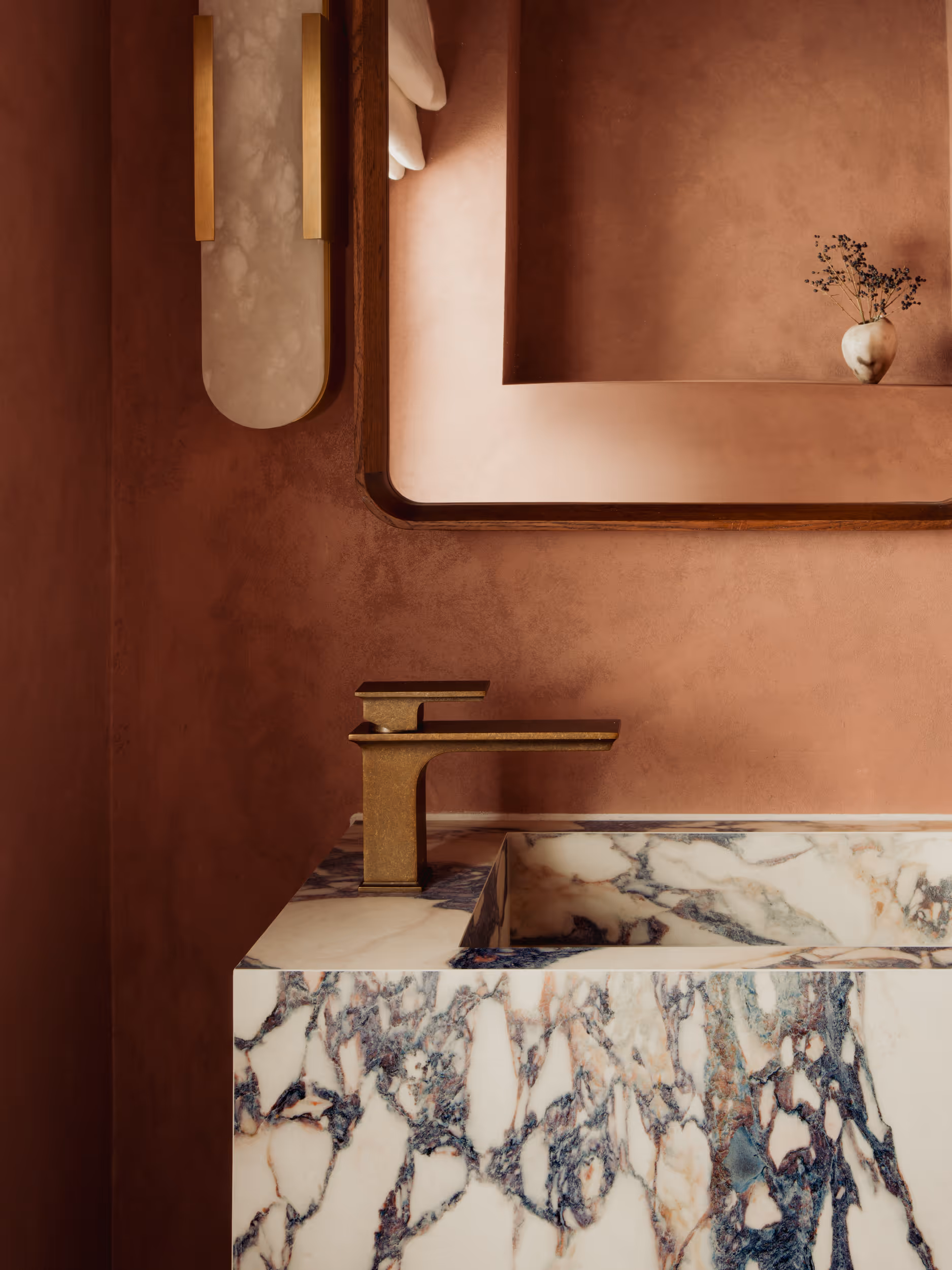 a large marble freestanding sink with gold hardware , the walls are limewashed in a burnt orange.