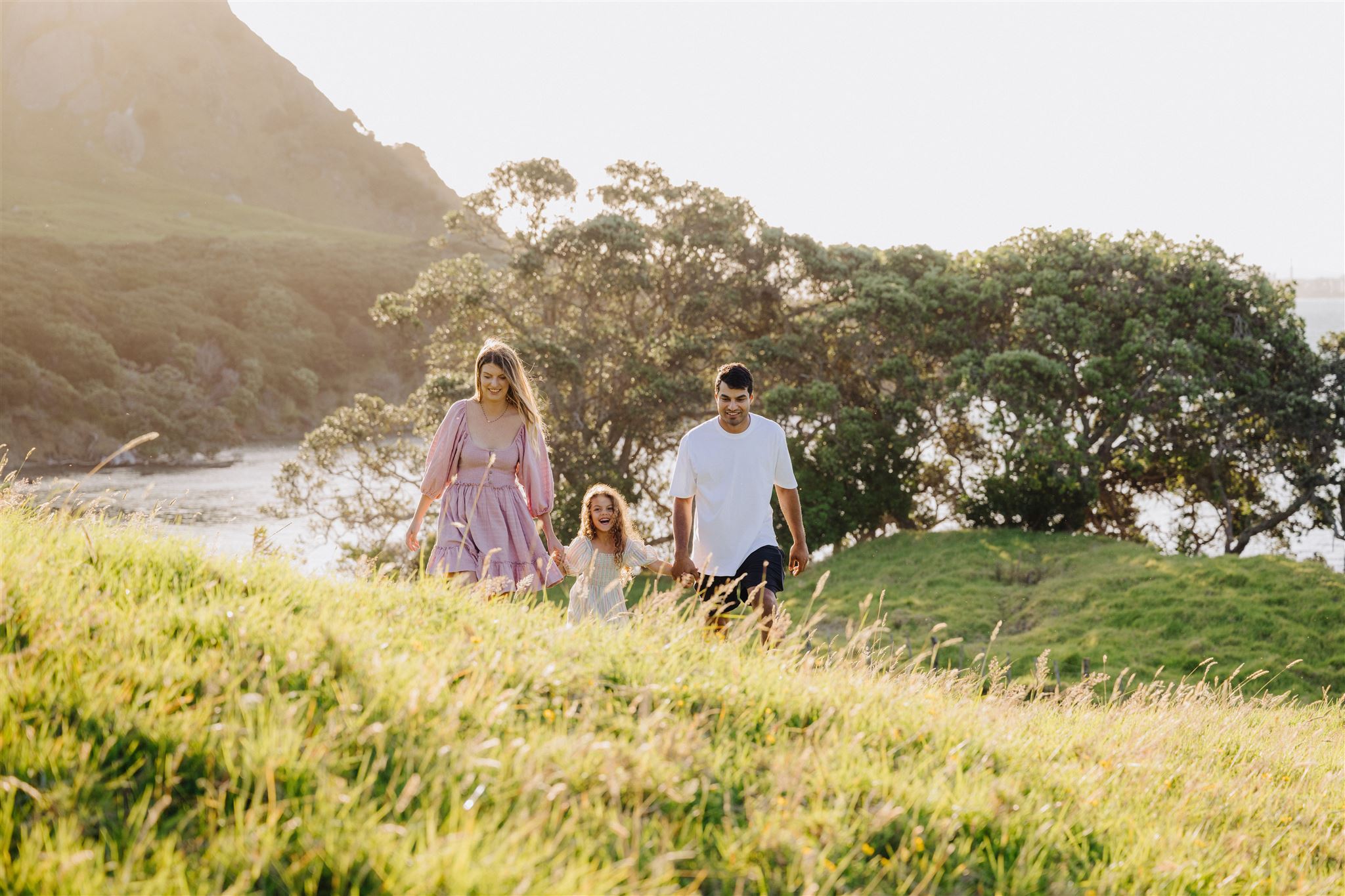 A family walking hand in hand through golden grass at sunset in Northland