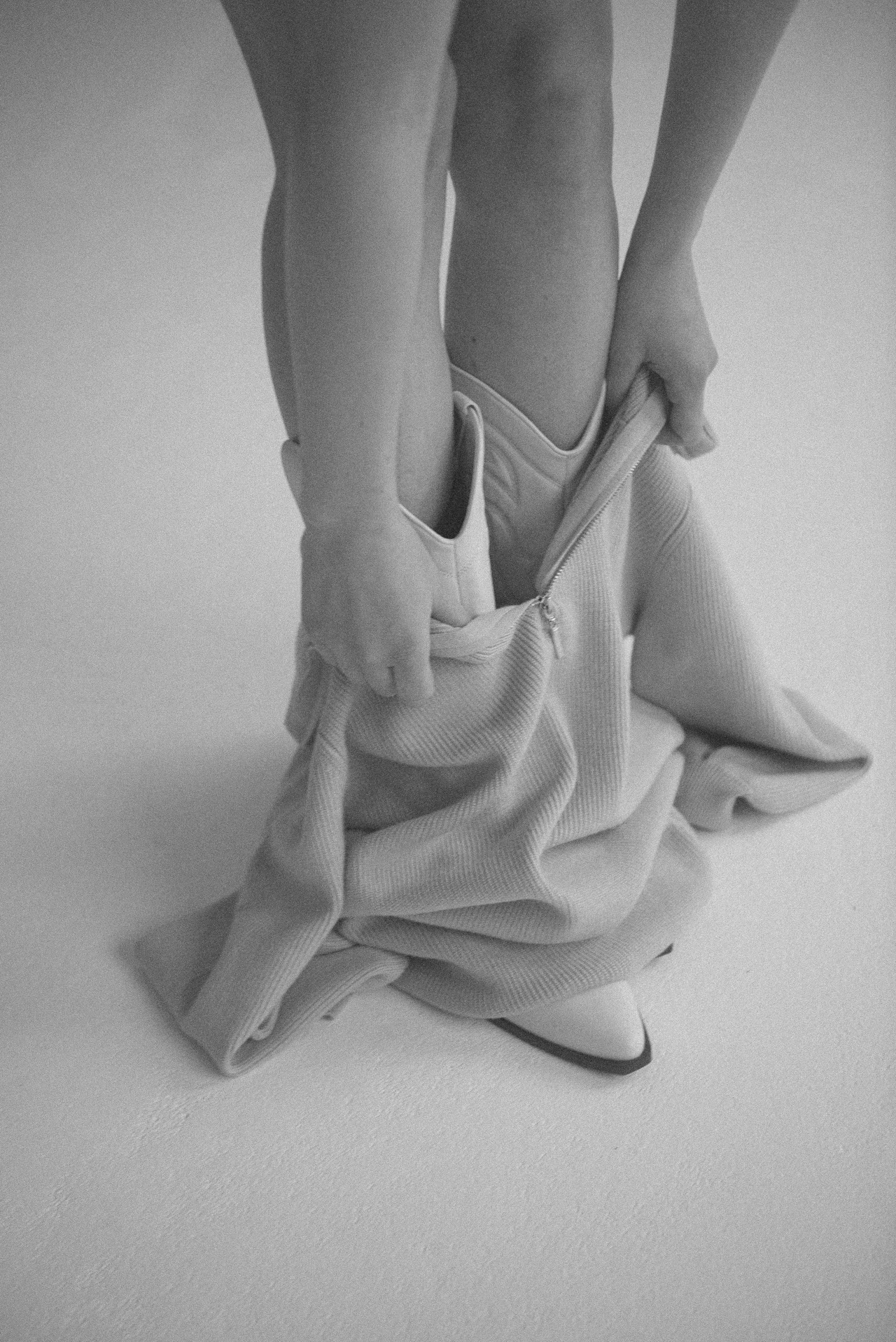 Person pulling down ribbed fabric pants while wearing pointed-toe ankle boots.