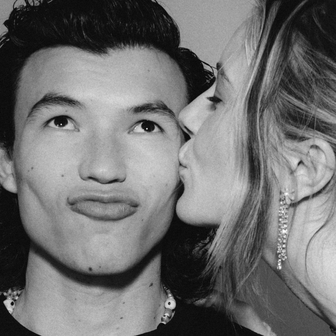 Black and white close-up of a woman kissing a man's cheek while he makes a playful duck face.