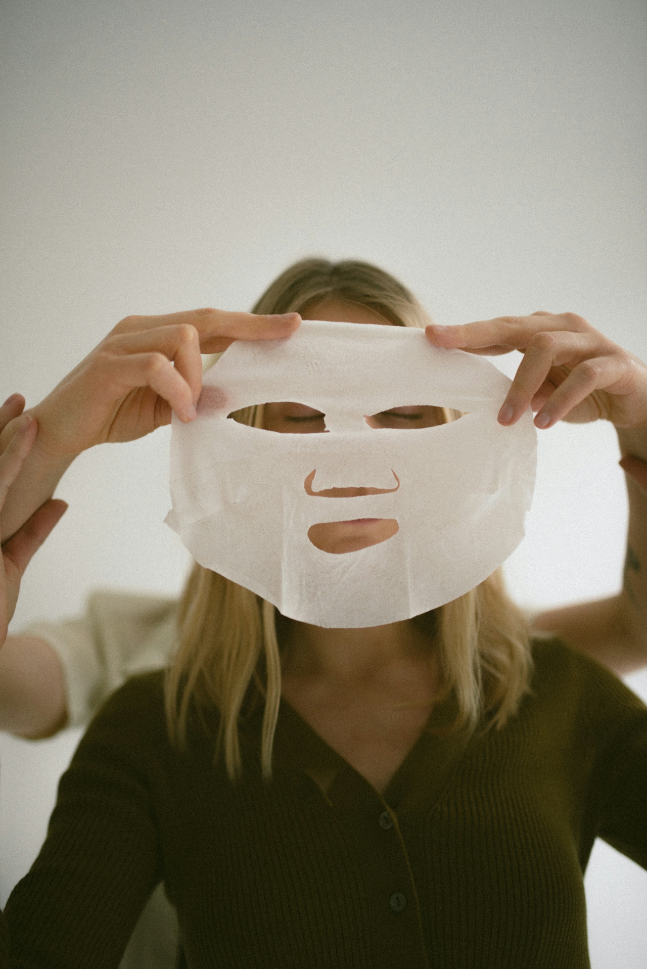 Woman holding a white sheet face mask in front of her face with eyes closed.