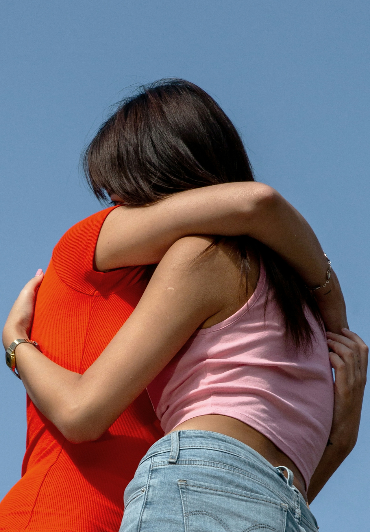Two women hugging each other tightly outdoors against a clear blue sky.