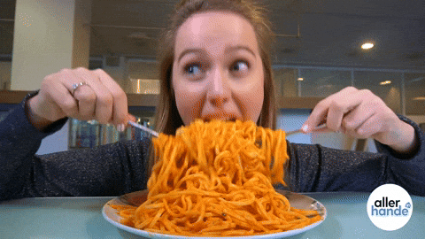 Woman enthusiastically eating a large plate of spaghetti with fork and spoon.
