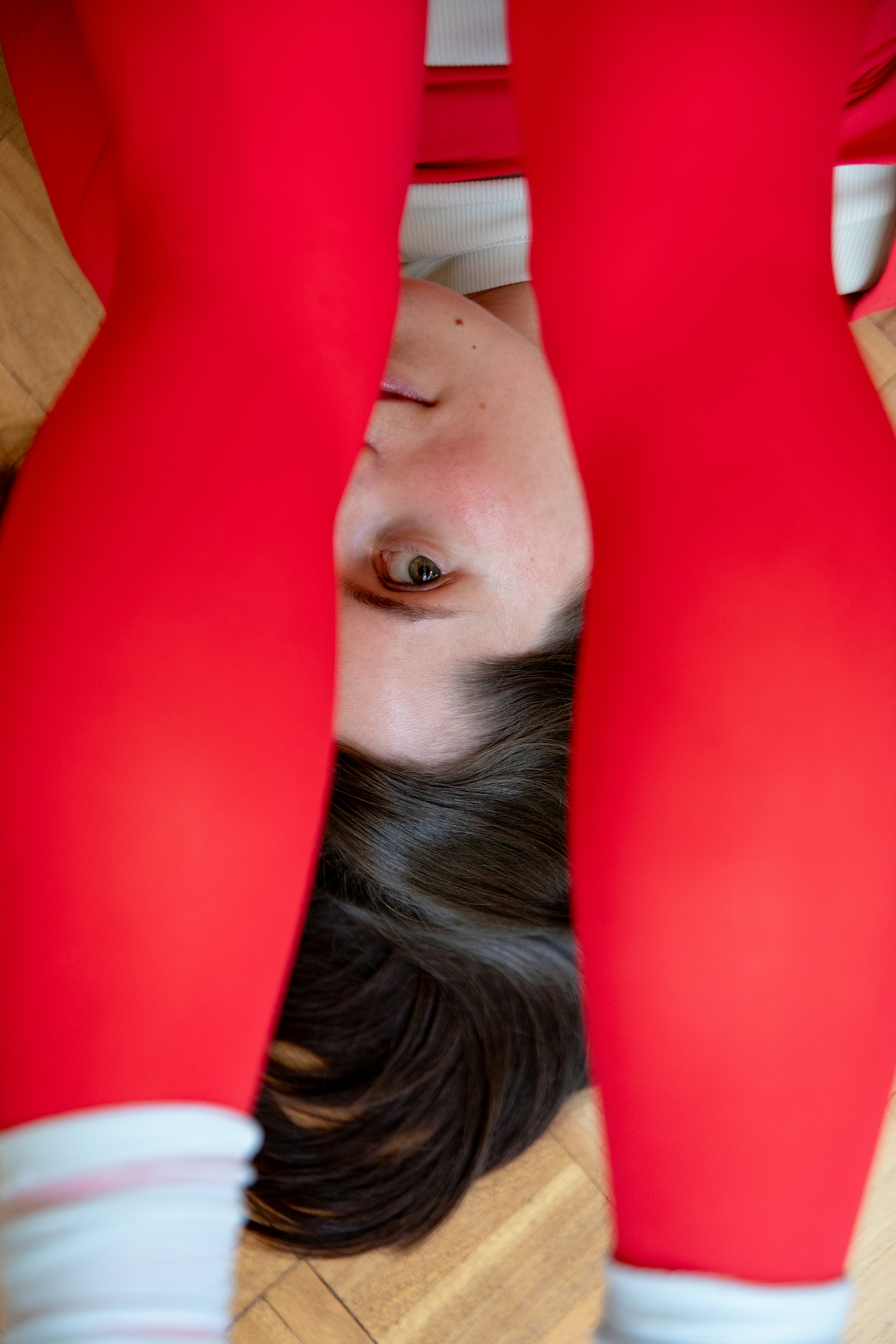 Close-up of a person lying on wooden floor with red leggings framing their face and dark hair spread out.