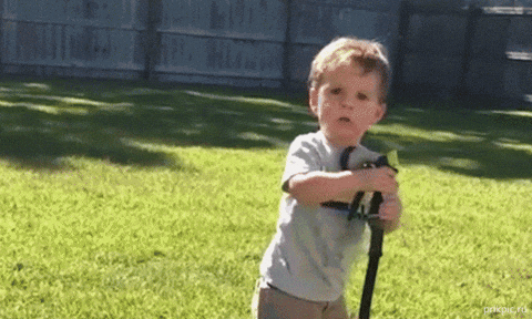 Young boy in gray shirt struggles to handle a garden hose that sprays water unexpectedly in a backyard.