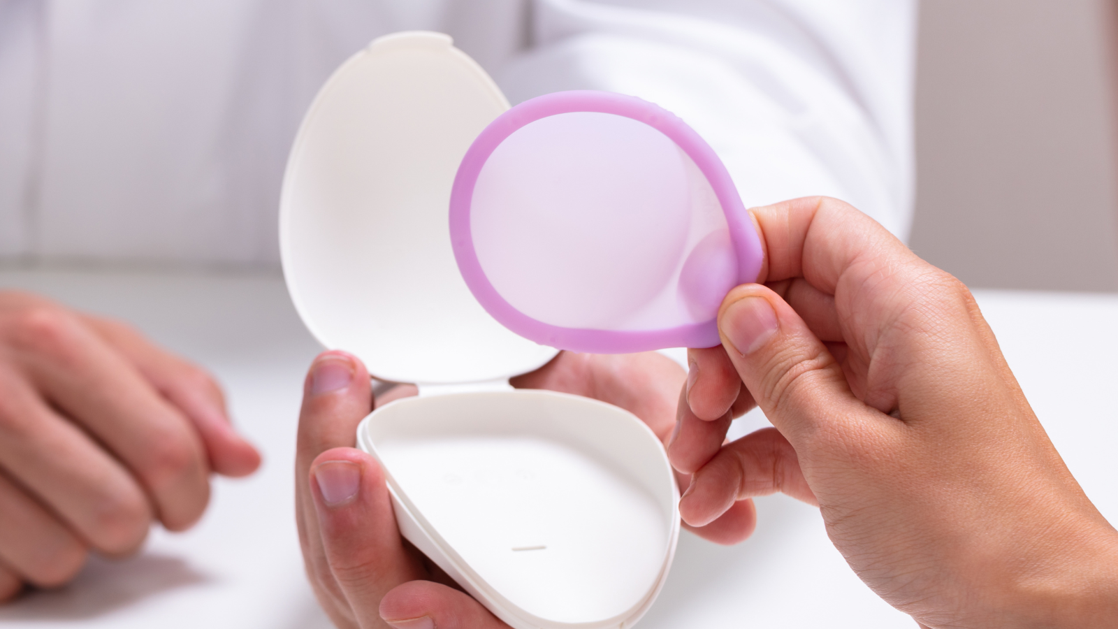 Person holding a purple silicone diaphragm contraceptive and its white storage case.