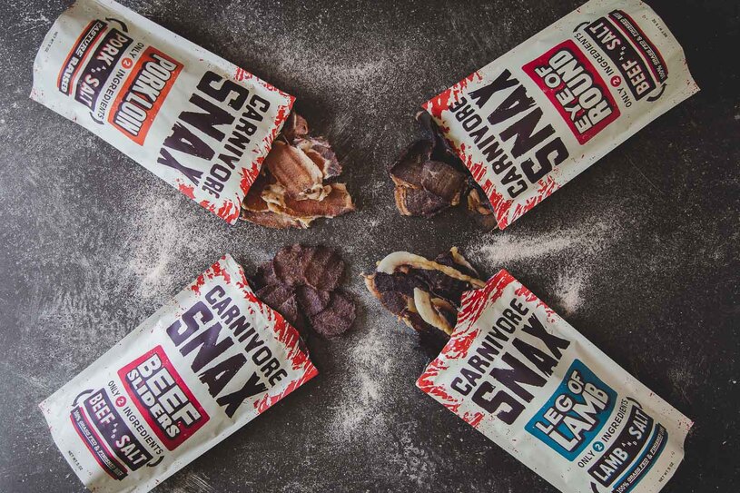 Carnivore Snax beef, pork, and lamb meat chips displayed on a dark surface