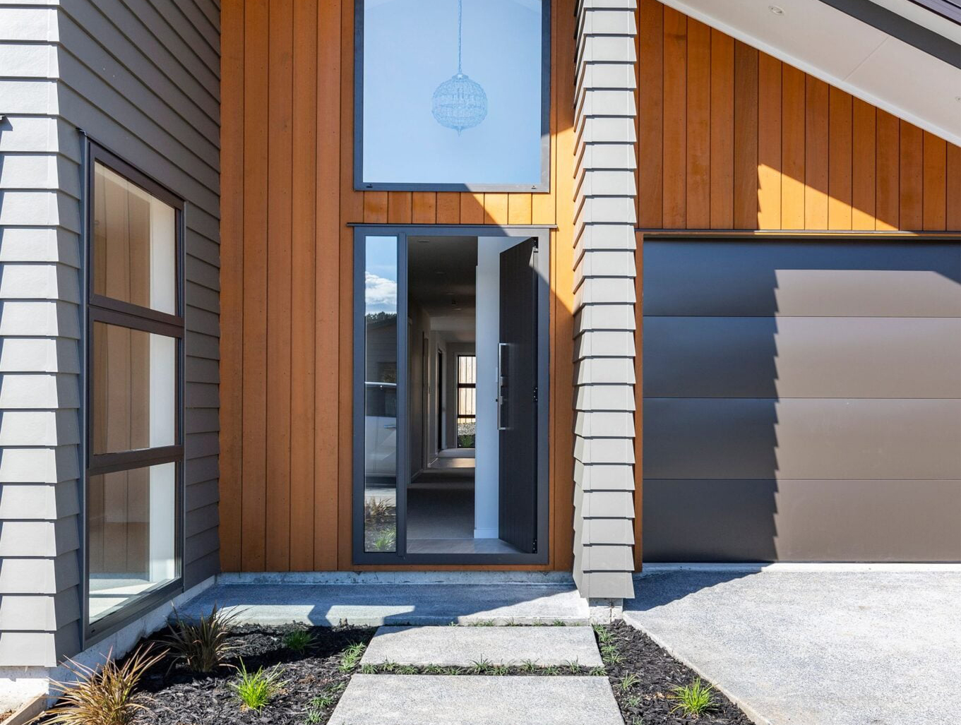 Modern home entrance featuring a sleek black aluminium front door by Rodney Aluminium, framed with vertical timber cladding and full-height sidelight for natural light and clean architectural appeal.