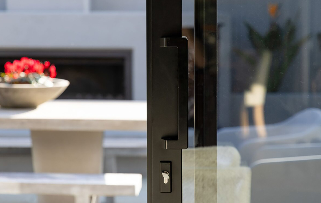 Close-up of premium black aluminium door hardware by Rodney Aluminium, installed on a glass wine cellar door with timber shelving and wine bottle display in the background.