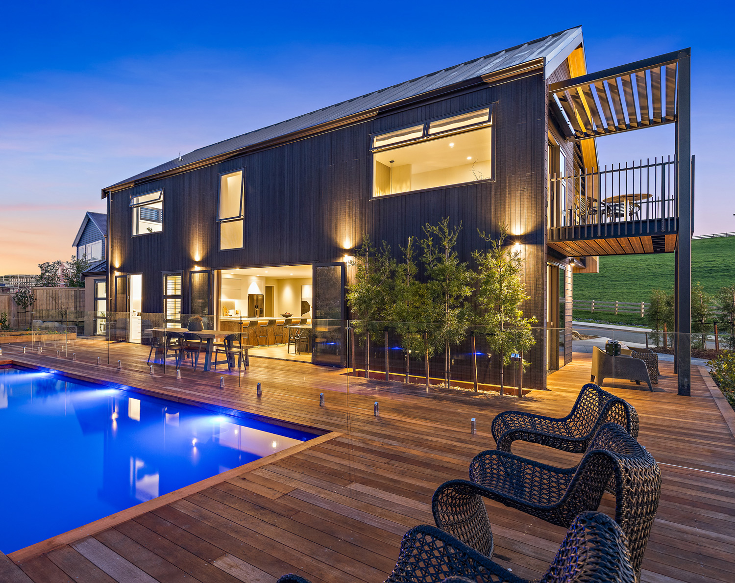Contemporary Whangarei home with black aluminium joinery, featuring sliding doors and windows opening onto a timber deck and illuminated swimming pool.