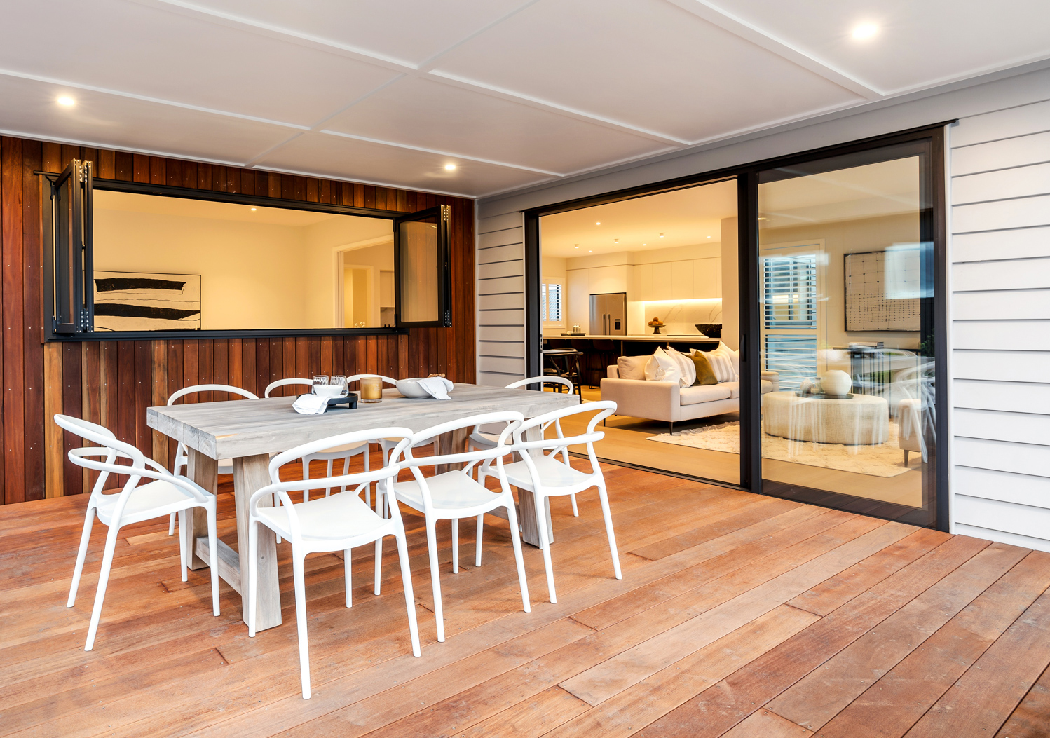 Modern Northland home with aluminium bifold servery window and sliding doors connecting indoor and outdoor living spaces over a timber deck.