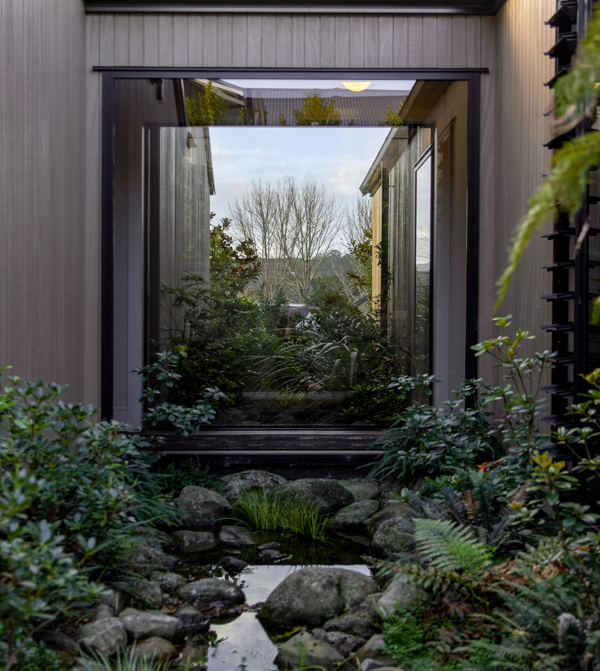 North Shore home featuring a large fixed aluminium window showcasing landscaped garden views with natural stone and native planting.