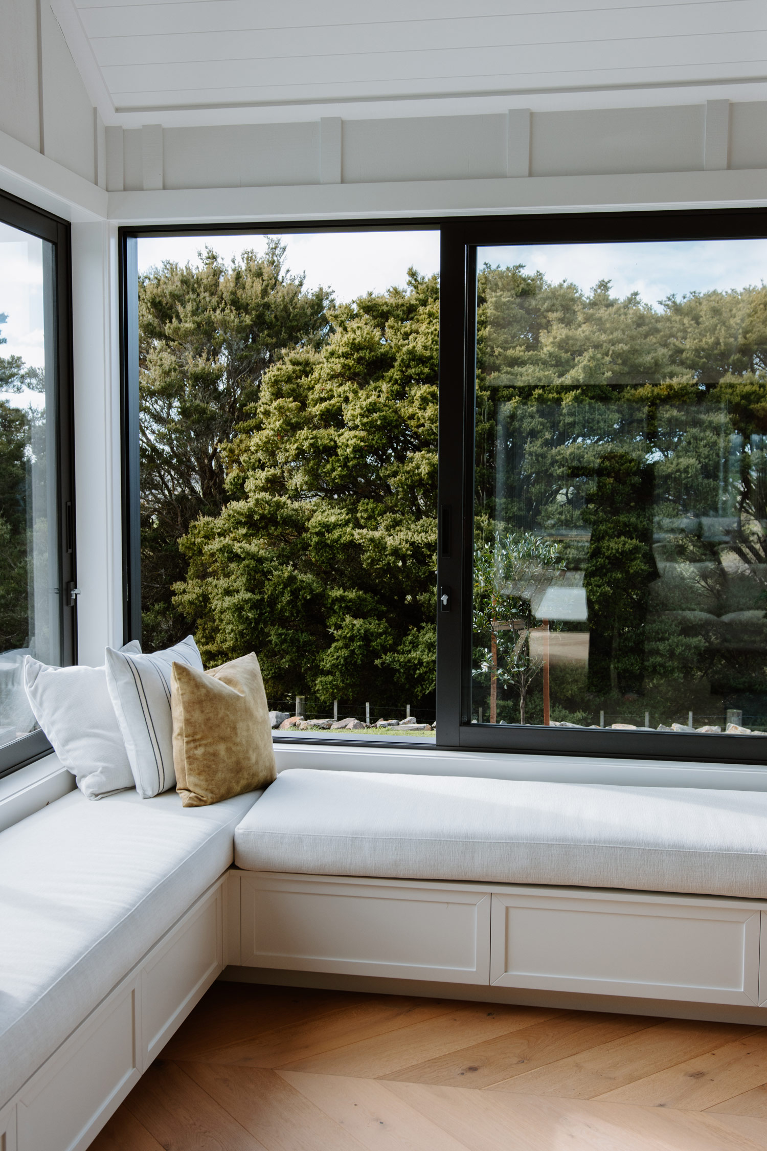 Modern corner window seat with large aluminium sliding and stacking windows by Rodney Aluminium, offering a scenic view of native bush in a New Zealand home