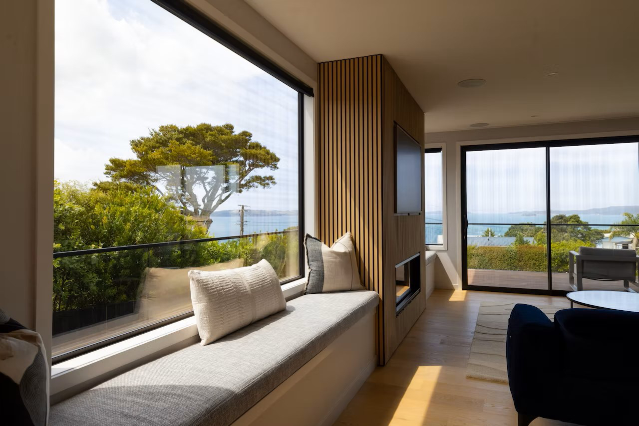 Contemporary living room with large tinted glass windows and sliding doors offering ocean views, designed for privacy and sun control – Rodney Aluminium NZ.