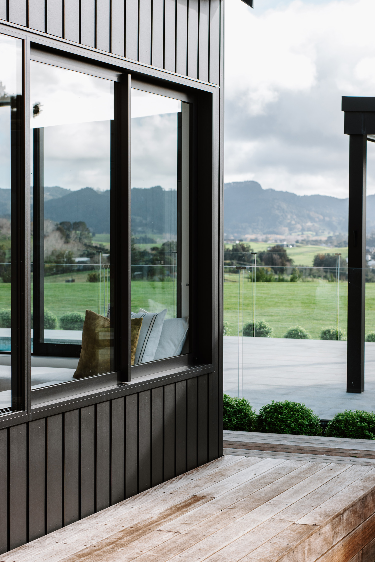 Close-up of modern black aluminium joinery window with vertical timber cladding, reflecting scenic rural views and showcasing premium window detailing in a Matakana home.