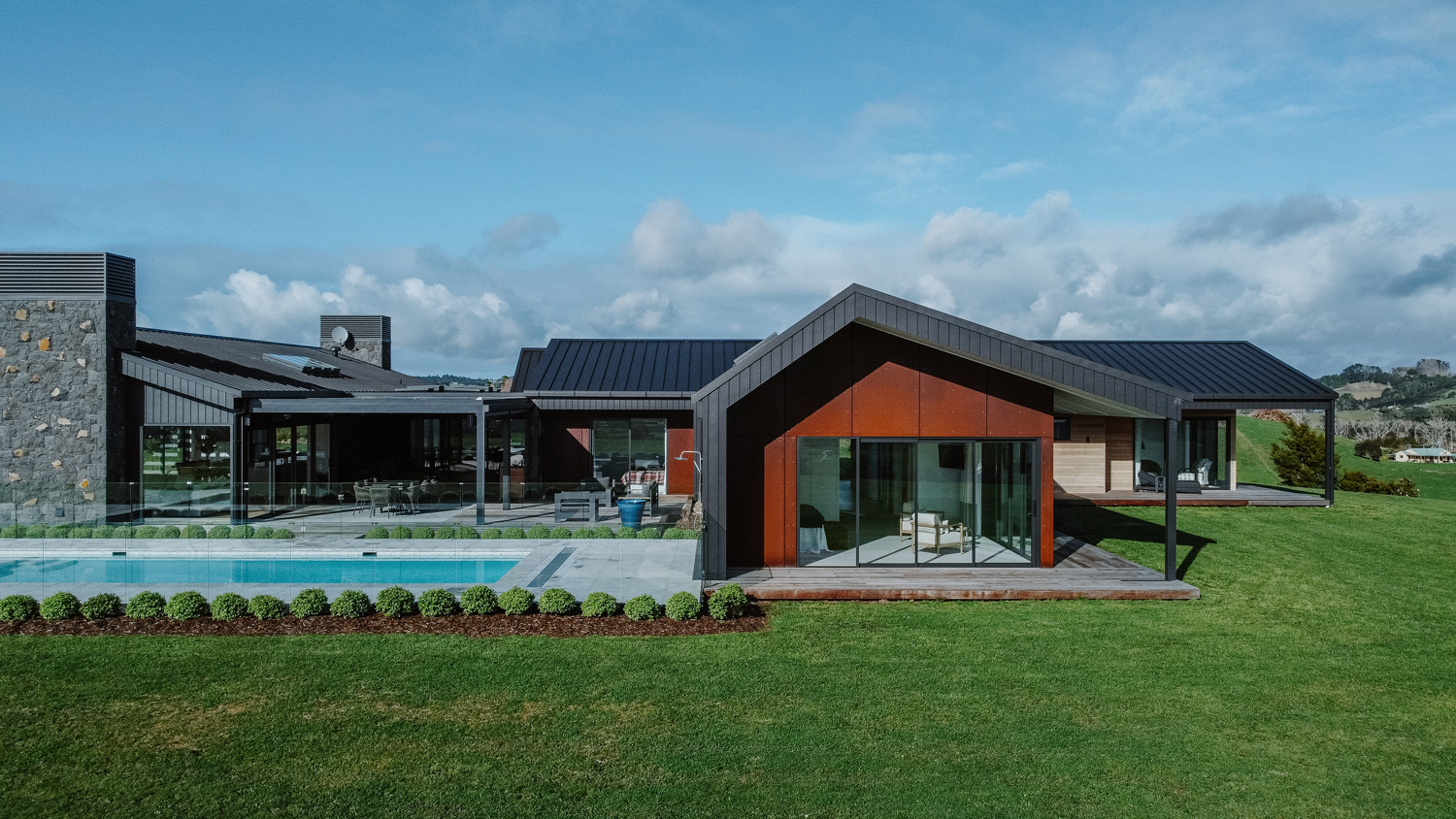 Architectural rural home in Matakana featuring large black-framed sliding doors and windows, modern cladding, and a poolside outdoor living area with aluminium joinery by Rodney Aluminium.