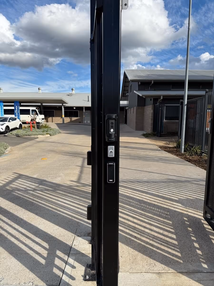 A black metal gate is open with a security keypad and intercom