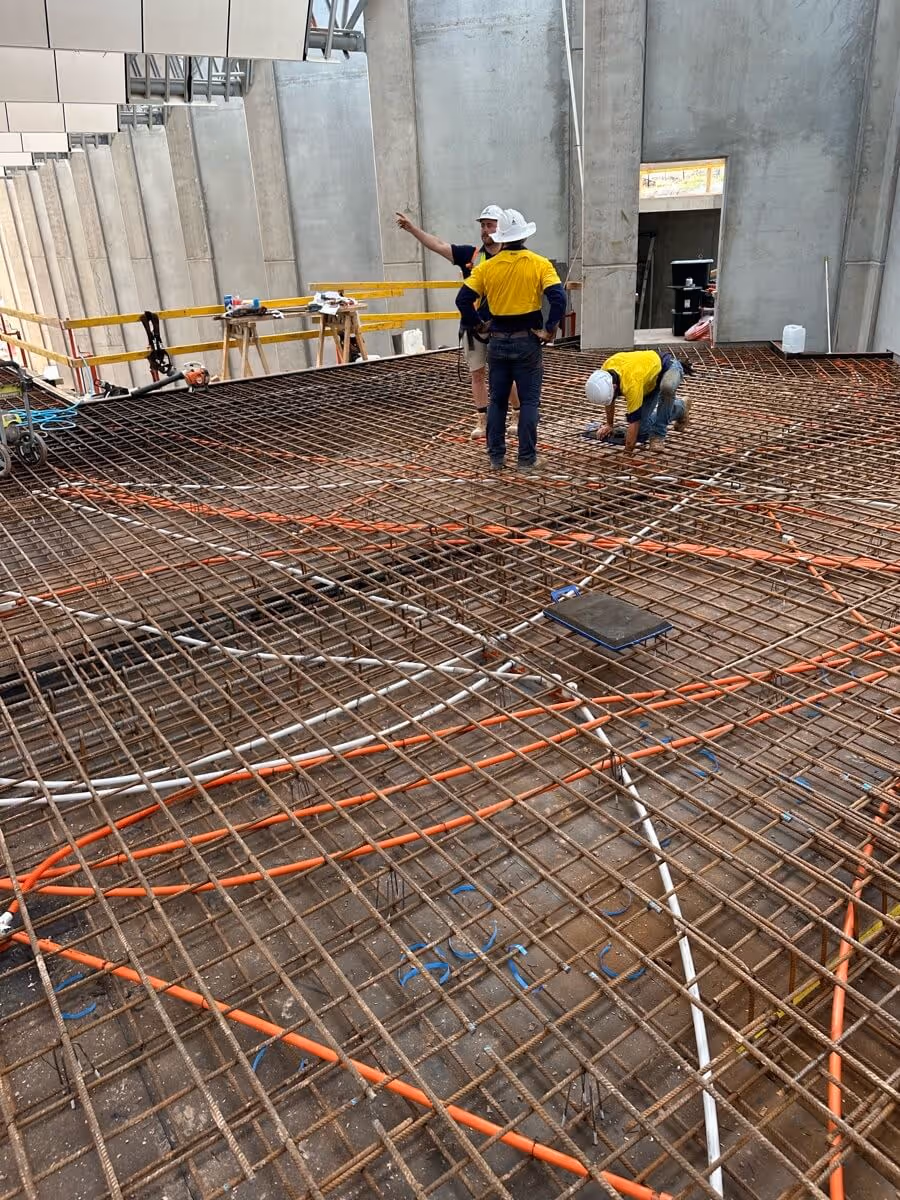 Construction workers in yellow vests stand on a rebar grid, preparing a concrete floor in an unfinished building