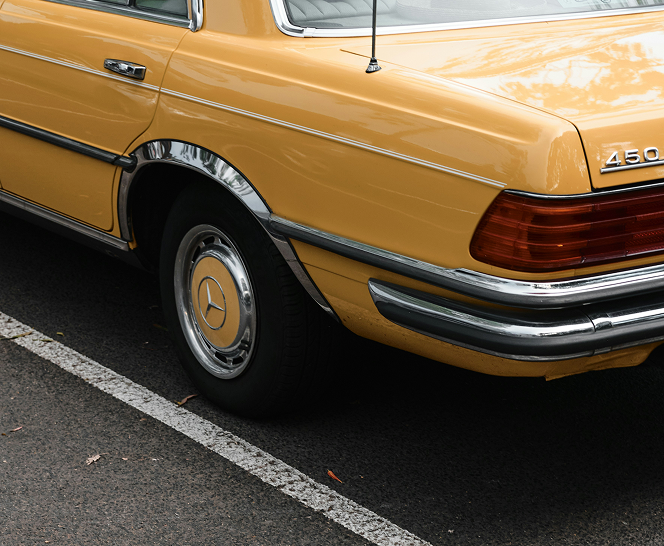 Rear view of a vintage mustard yellow Mercedes-Benz parked on asphalt.