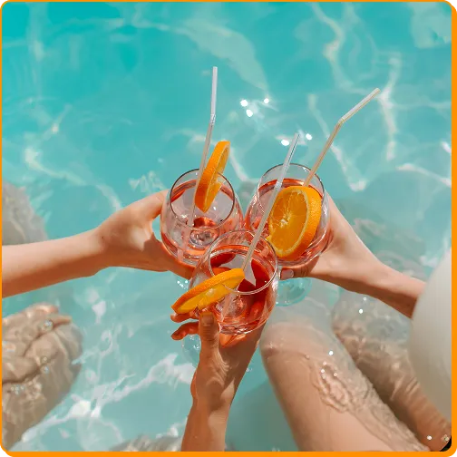 Three people toasting with orange-garnished drinks in a turquoise swimming pool.
