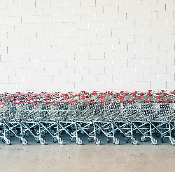 A long row of nested metal shopping carts with red handles against a white brick wall.