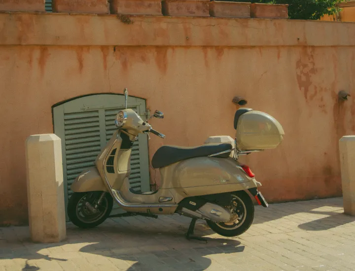A beige motor scooter parked in front of a sun-drenched terracotta wall.