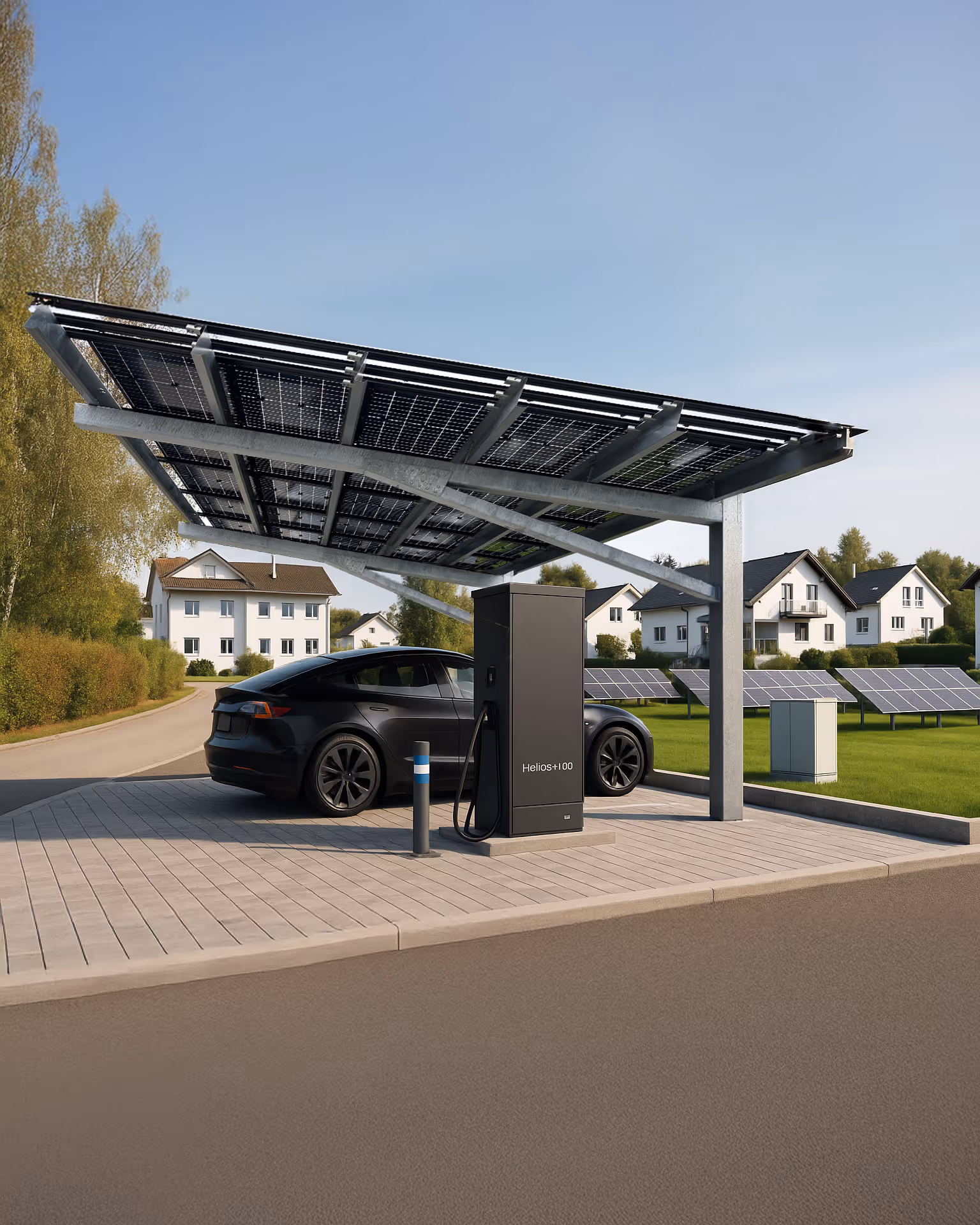 Ein elegantes schwarzes Elektroauto lädt unter einem einspurigen Solar-Carport mit integrierten Photovoltaikmodulen, beschriftet mit „Helios+100“. Die Anlage steht auf einem ordentlich gepflasterten Bereich neben einer Strasse in einem Vorort mit weißen Häusern und gepflegten Rasenflächen. Im Hintergrund sind bodenmontierte Solarpanels und Bäume unter einem klaren blauen Himmel zu sehen.