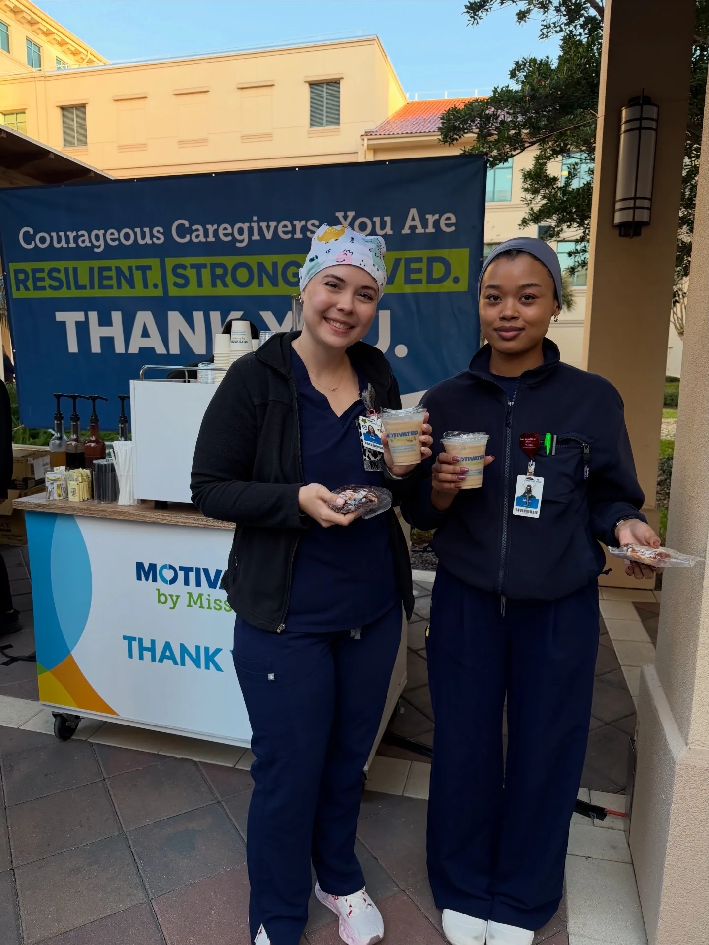 AdventHealth caregivers holding branded drinks by the Motivated by Mission cart and Courageous Caregivers Thank You banner