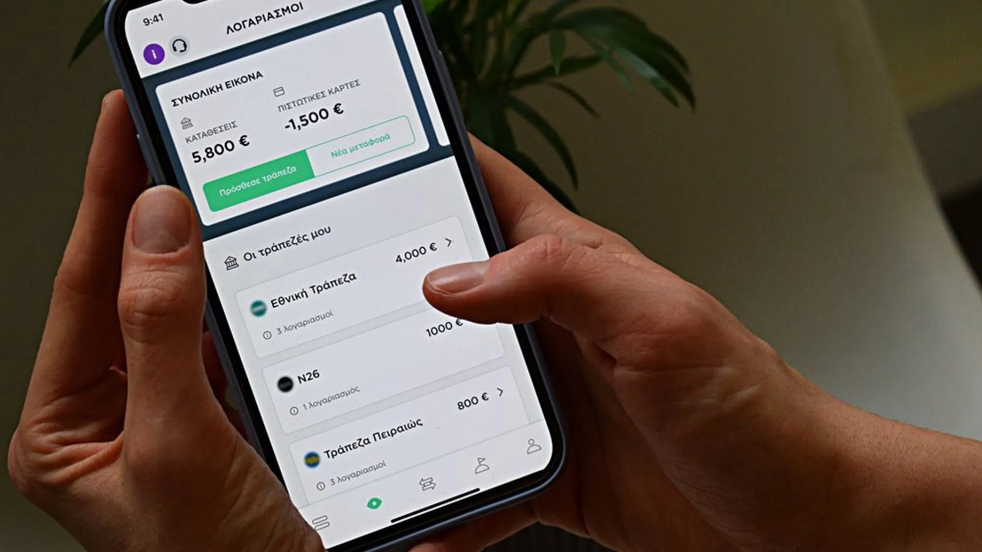 User holding phone with Waiz app showing account balances in Greek.