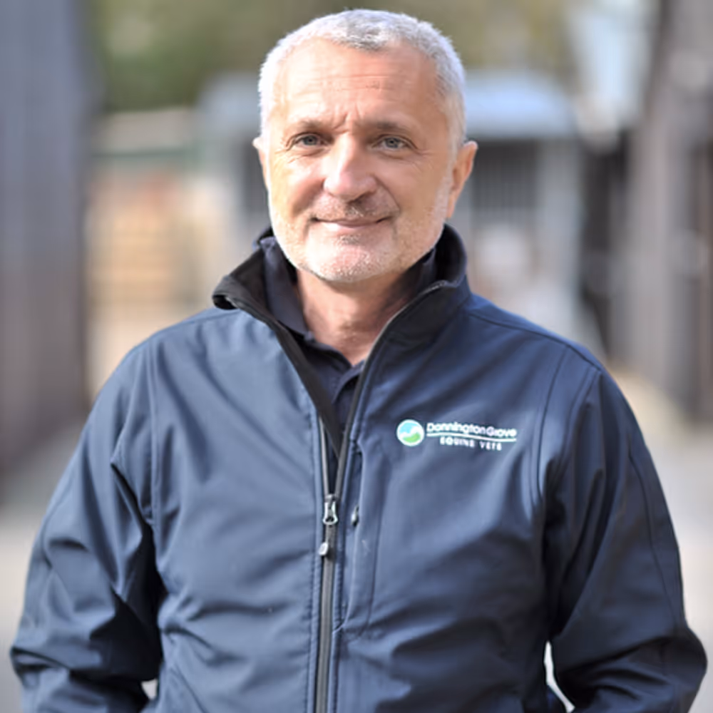 Smiling Giorgio Ricardi with short gray hair wearing a navy jacket with Donnington Grove Equine Vets logo.