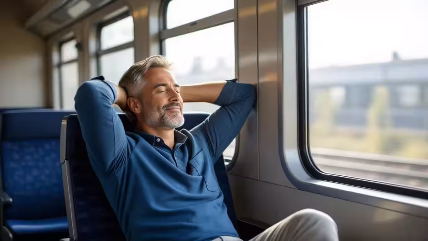 Man sitting on a train with head rested in hands behind his head.