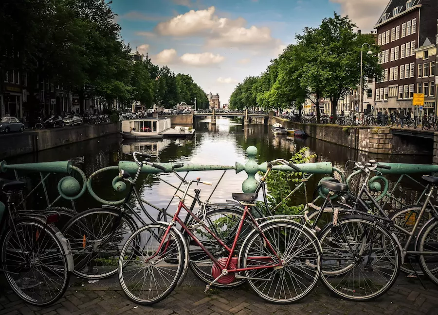 Bicycles parked along an Amsterdam canal with traditional houses