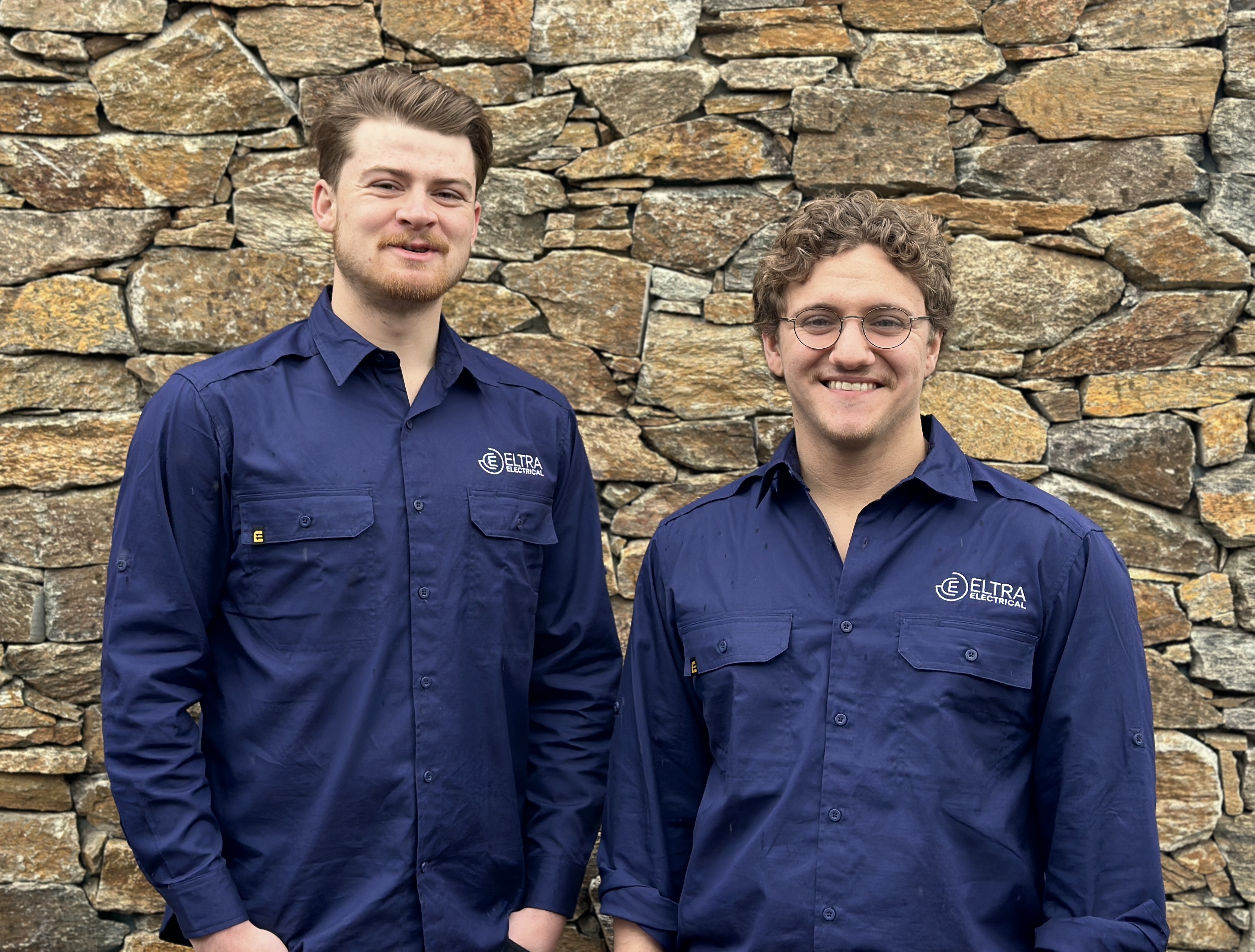 The Eltra Electrical team standing together in uniform, smiling confidently in front of a job site, representing professionalism and teamwork.