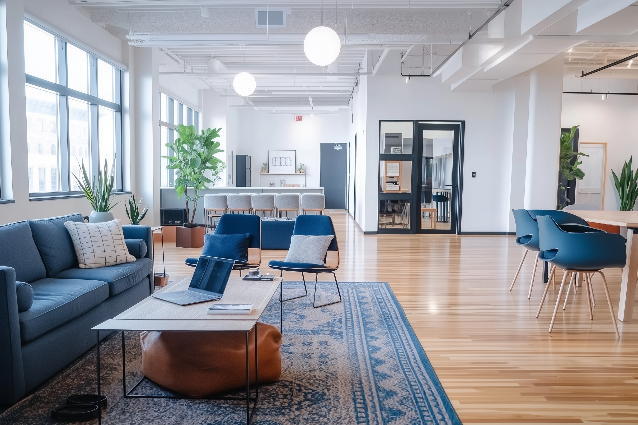 Modern commercial interior with blue sofa and chairs, wooden tables, large windows, green plants, bright pendant lighting, and light wood flooring.
